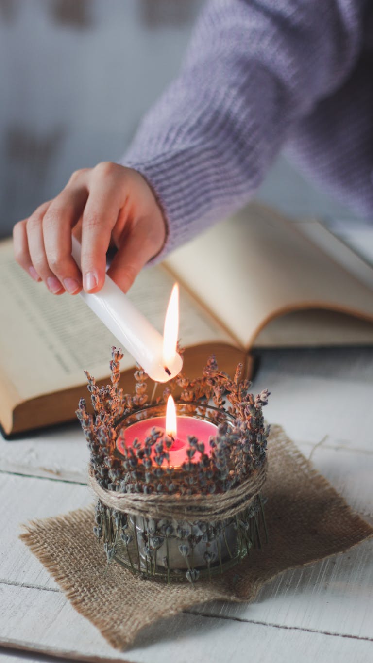 A hand lighting a decorative candle beside an open book on a rustic table.