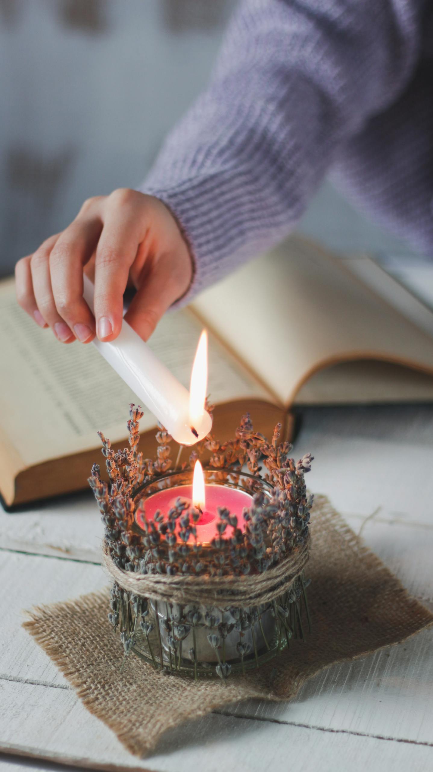 A hand lighting a decorative candle beside an open book on a rustic table.